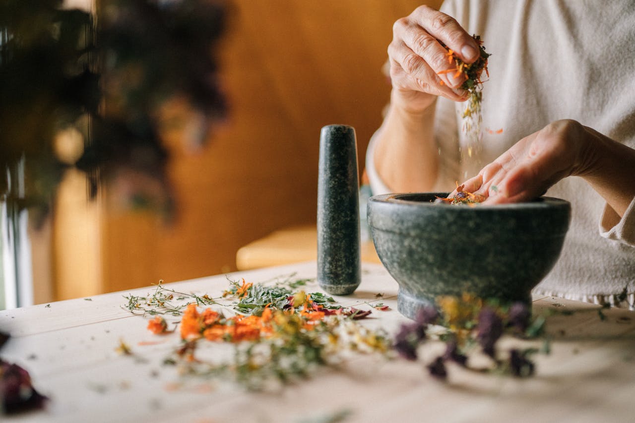 Close-up of hands grinding herbs and flowers in a mortar for natural remedies.